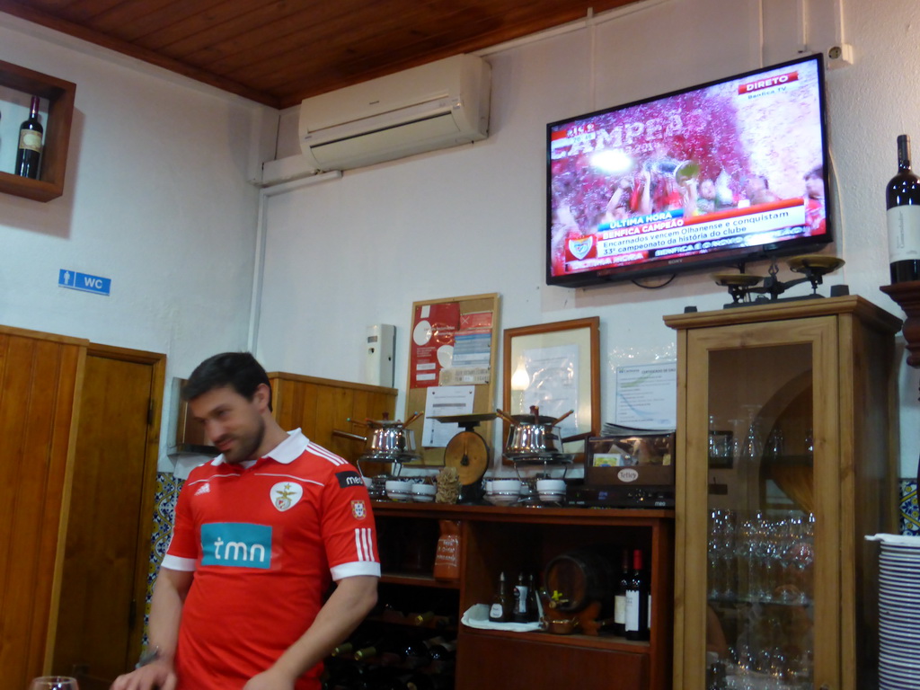 Waiter and TV with images of the championship of the S.L. Benfica soccer team at the A Gina Restaurant