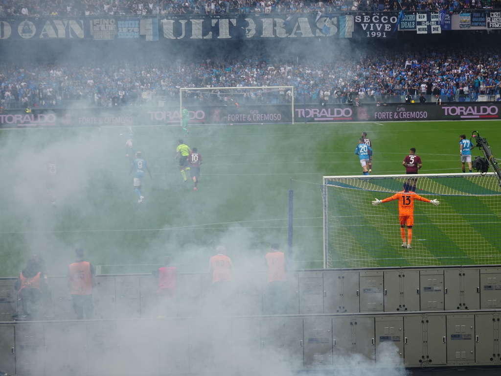 Players on the pitch and smoke at the Stadio Diego Armando Maradona stadium, viewed from the Curva A Inferiore grandstand, during the football match SSC Napoli - Salernitana