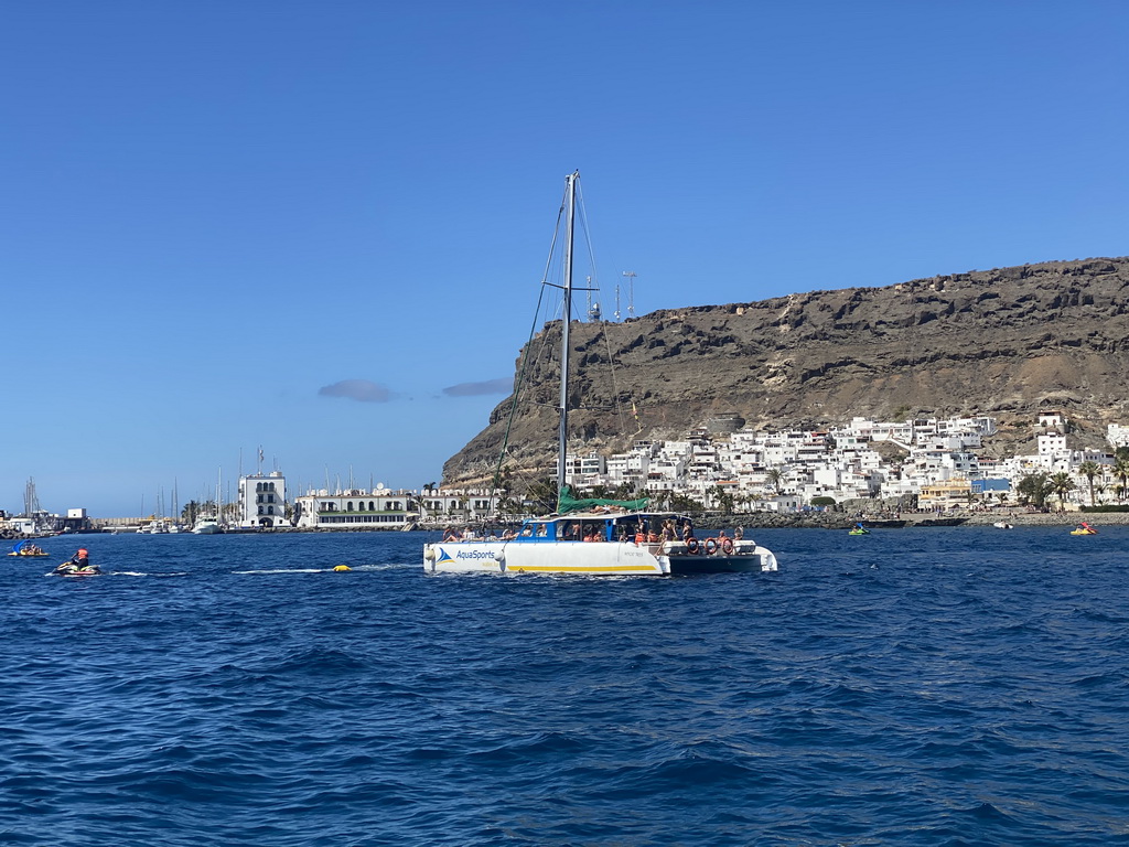 Boat and jet ski in front of the town center with the harbour and the Hotel THe Puerto de Mogán, viewed from the Sagitarius Cat boat