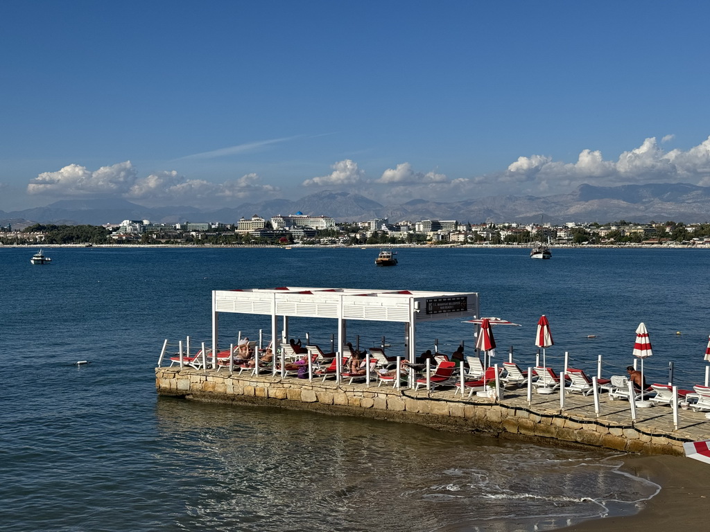 Pier at Nar Beach 1, boats in the Gulf of Antalya and beaches and hotels at the northwest side of town, viewed from the seaside path near the Turgut Reis Caddesi street