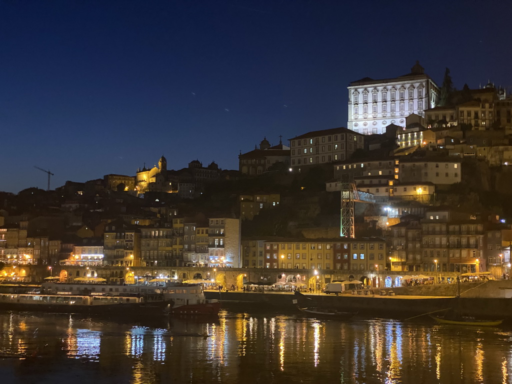 Boats on the Douro river and Porto with the Cais da Ribeira street, the Igreja de Nossa Senhora da Vitória church and the Paço Episcopal do Porto palace, viewed from the Avenida de Diogo Leite street, by night