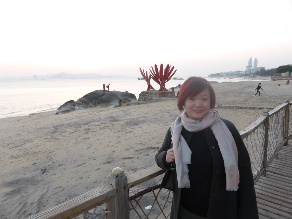 Miaomiao with a piece of art at the beach at Huandao South Road, two skyscrapers under construction and the South China Sea